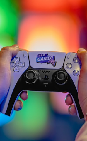 Two hands are holding a gaming controller labeled 'Pro Gamer'. The background is blurred with colorful lights creating a vibrant atmosphere.